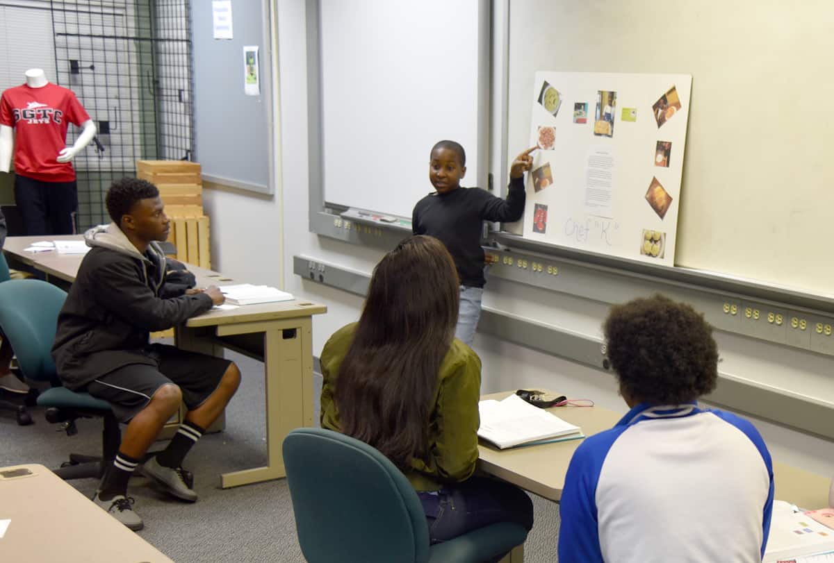 Kaylon Harvey is shown pointing to a poster board in front of a class of college students.