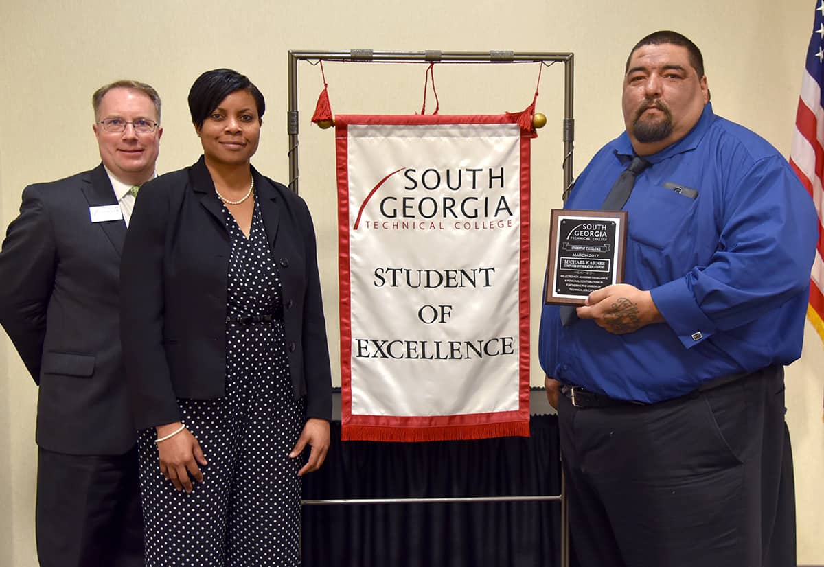 Michael Karnes (far right) is pictured with Vice President for Academic Affairs David Kuipers and his nominating instructor Andrea Ingram and the Student of Excellence banner that will hang in the Computer Information Systems program area until the next Student of Excellence is named.