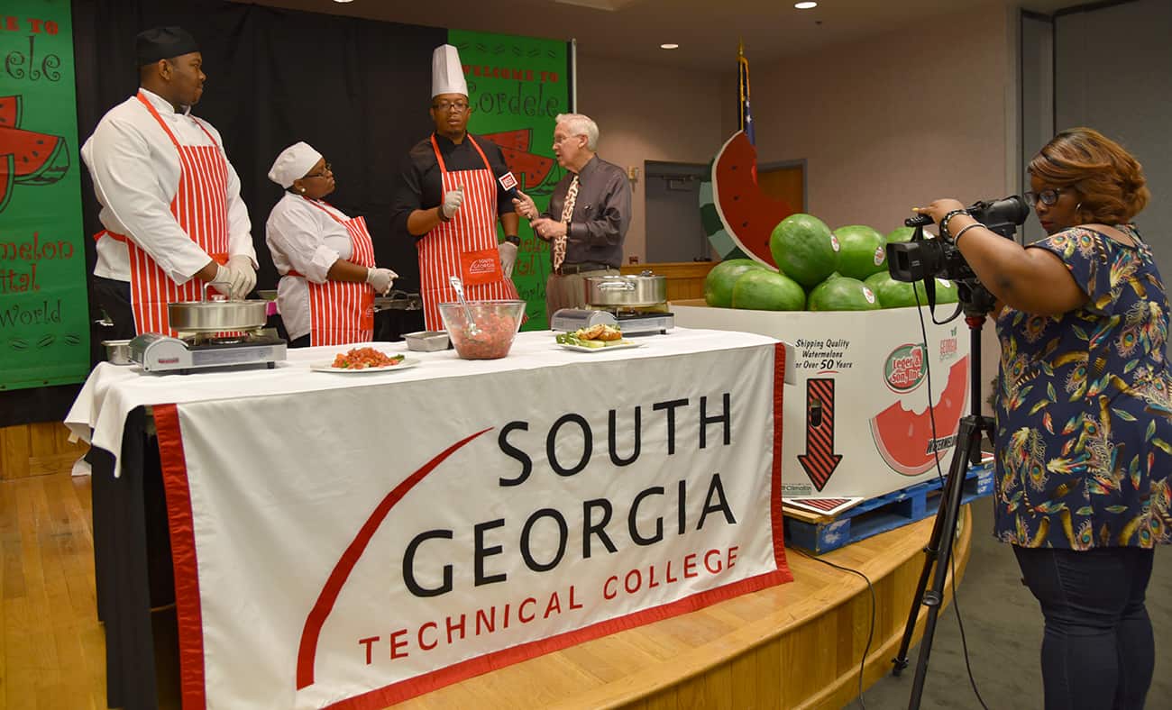 SGTC Culinary Arts instructor Johnny Davis (third from left) is pictured while being interviewed by WSST-TV’s Phil Streetman after the cooking demonstration he and his students gave for the Cordele Watermelon Days Festival. Culinary Arts students Esau West and Qundra Ford, also pictured, assisted with the demonstration.