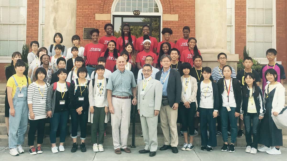 Lady Jets, Mayor Barry Blount and the Japanese delegation pose in front of building