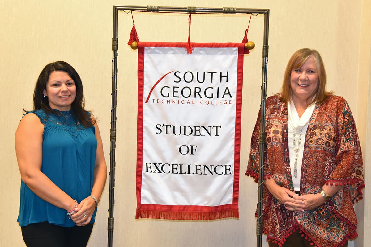 Student of Excellence winner Melisa Flakes stands with nominating instructor Jaye Cripe beside the Student of Excellence Banner.