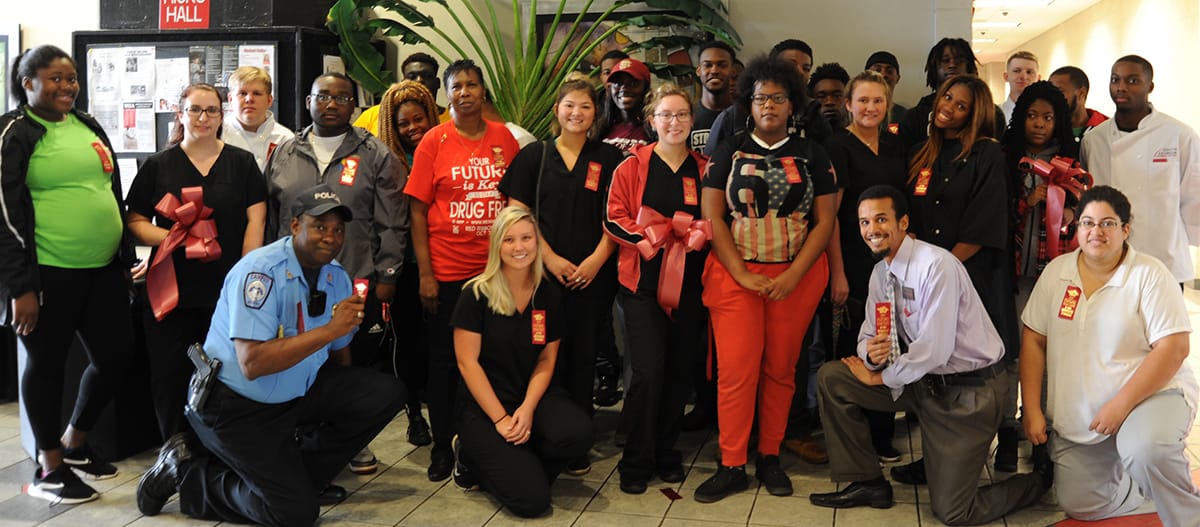 Group photo of some faculty and staff with students wearing red ribbons and a few students holding big red bows.