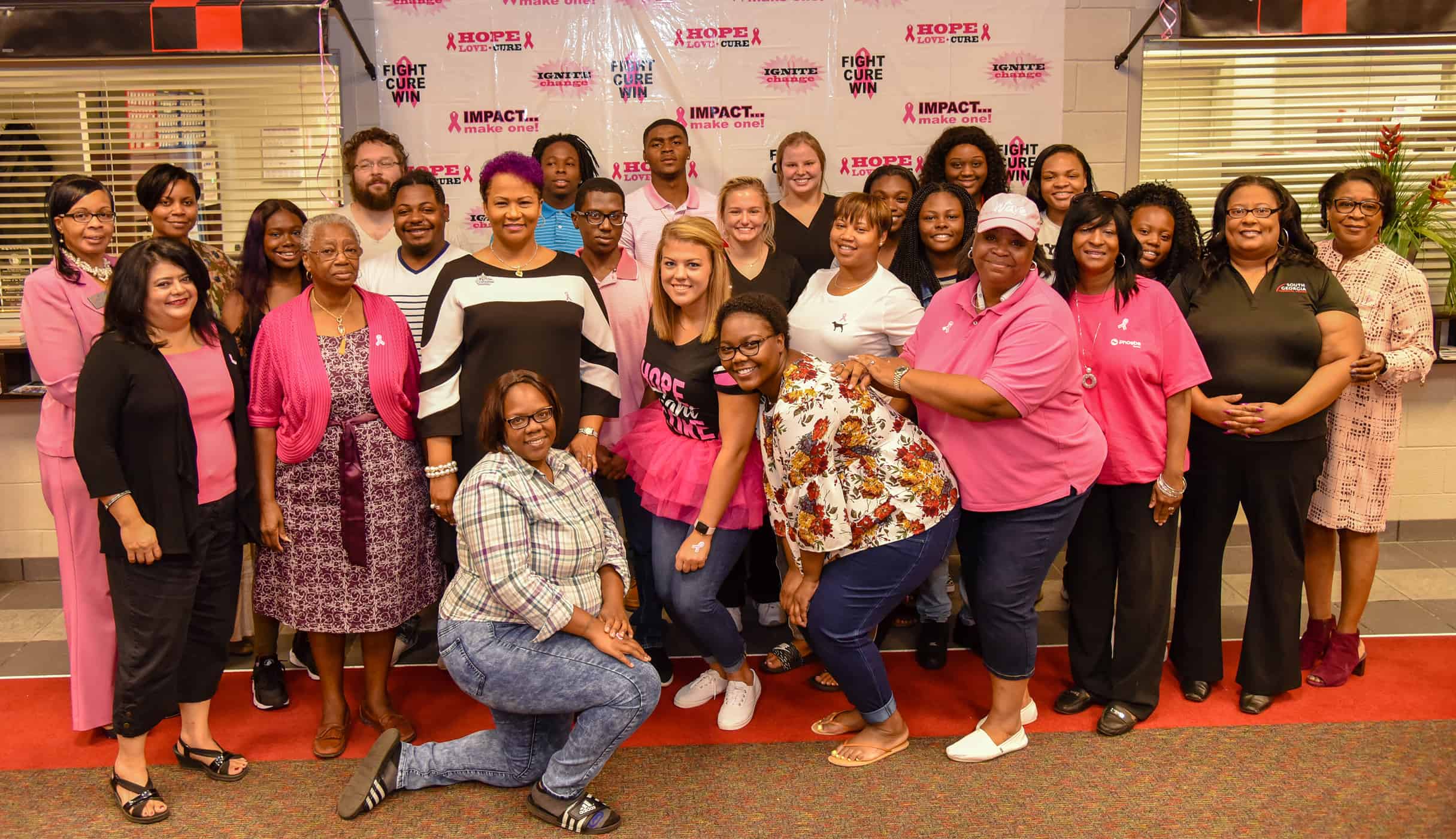 A group of 27 people, many wearing pink, stand together for a picture.