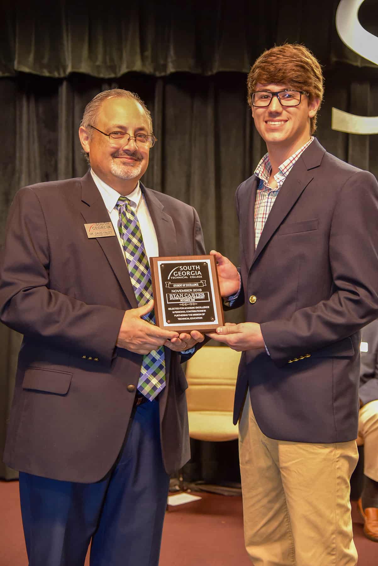 A man accepts a plaque from another.
