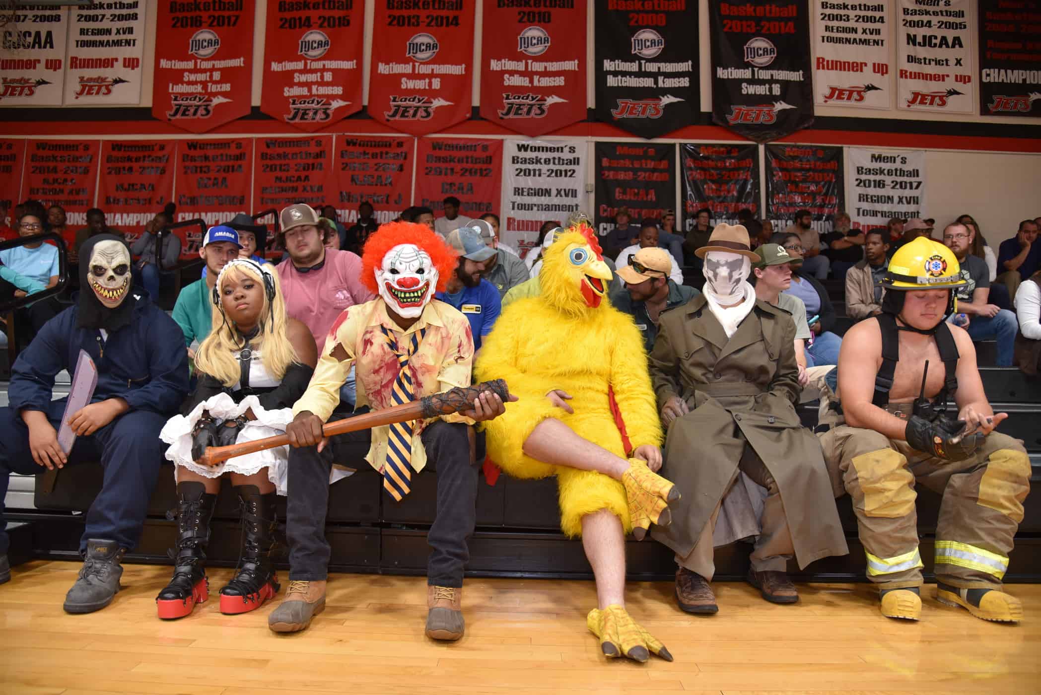 A group of costumed people sit on the front row of bleachers