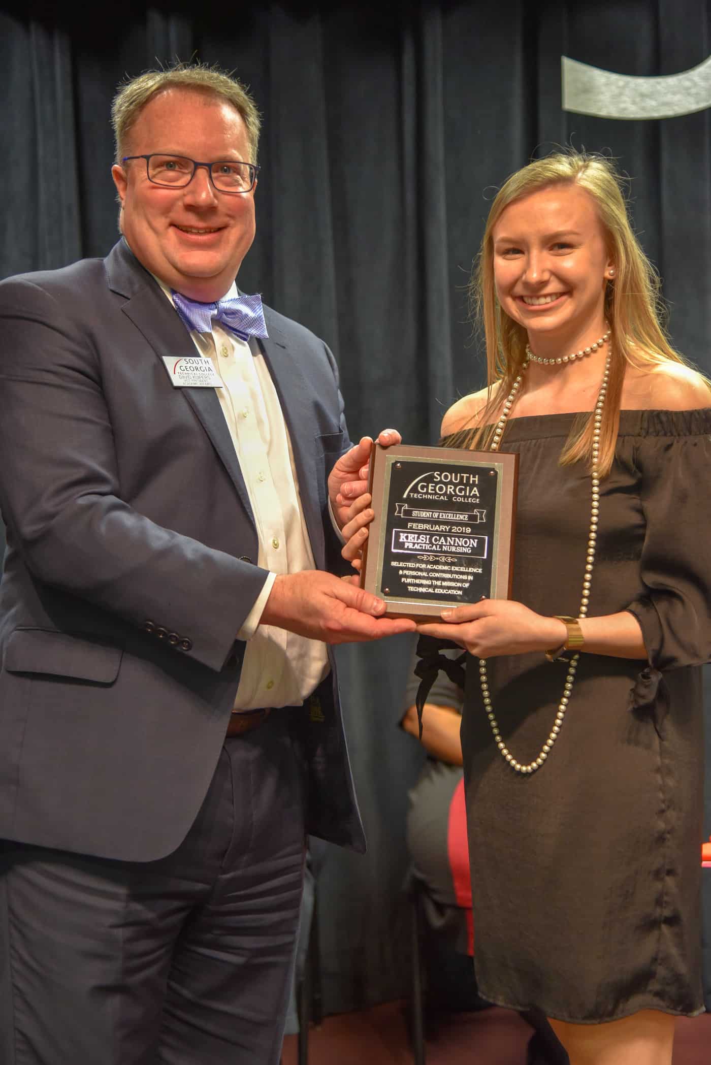 A female stands on the right and accepts a plaque from a man on the left