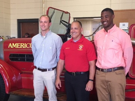 Three men stand in front of an old fire engine.