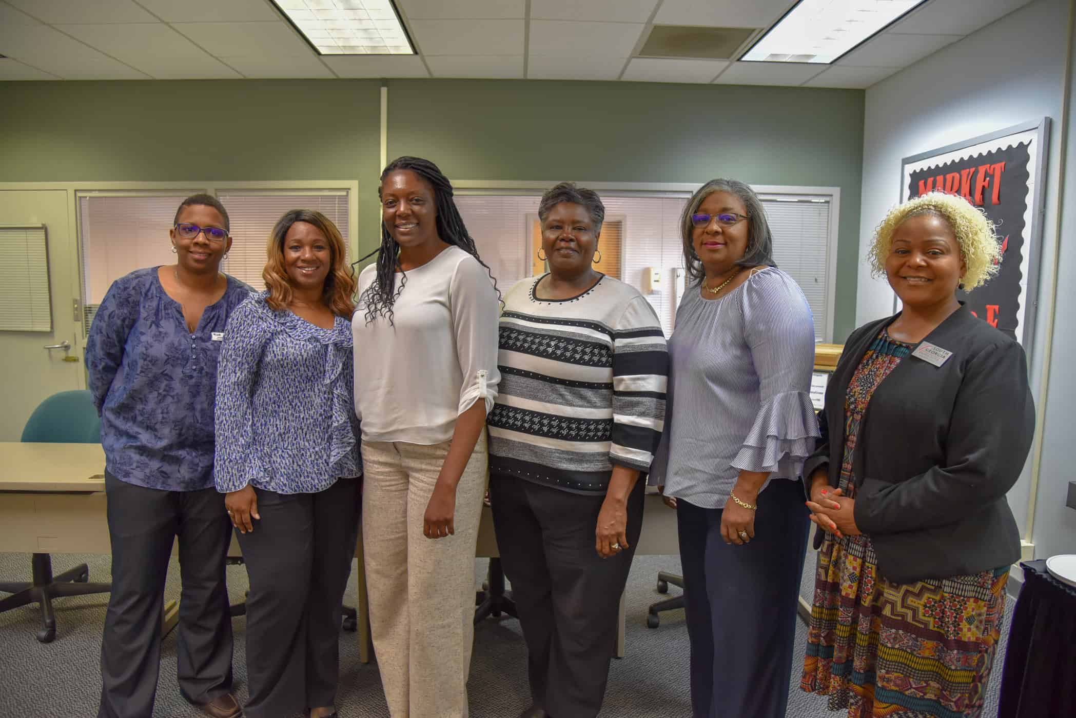 Six women stand together, side by side facing the camera.