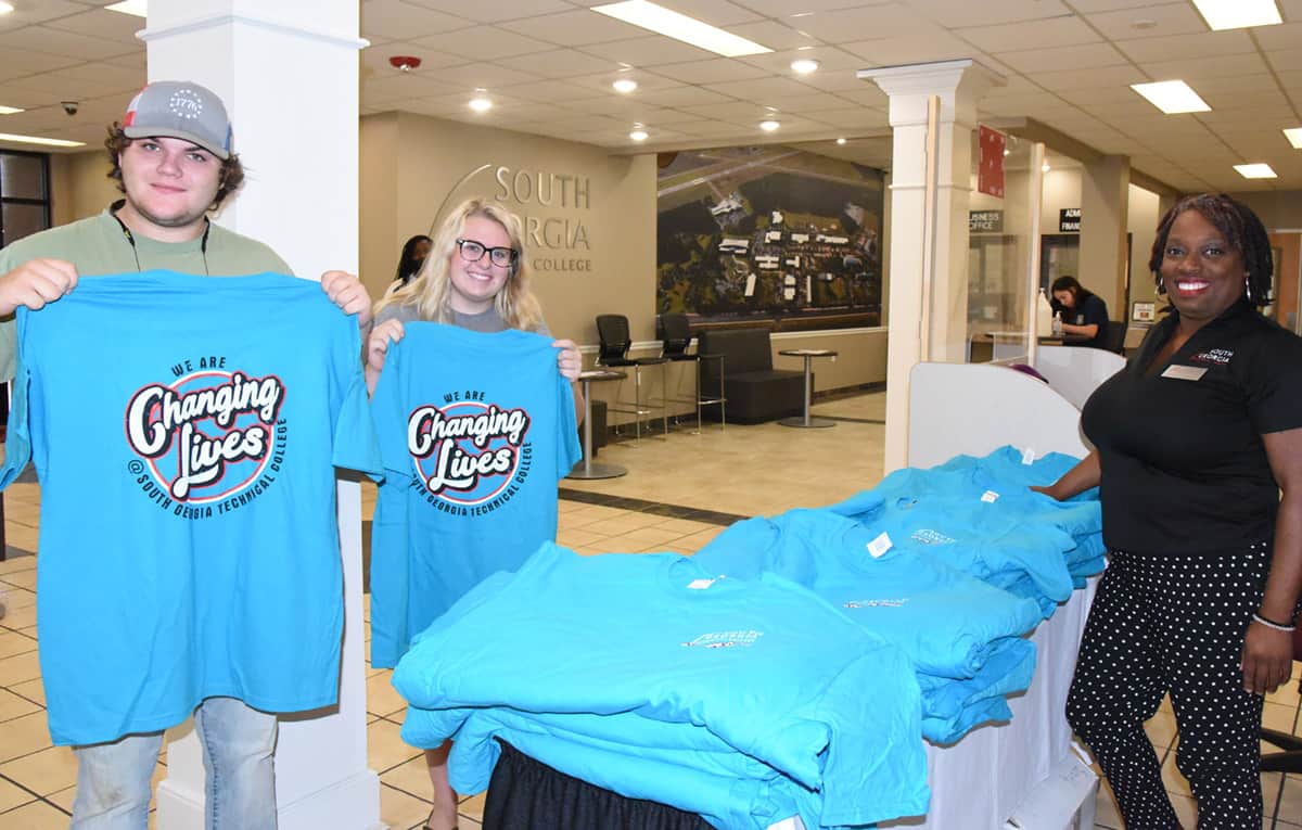 Two students receive t-shirts from SGTC Special Services Coordinator Jennifer Robinson at the college’s July registration day.